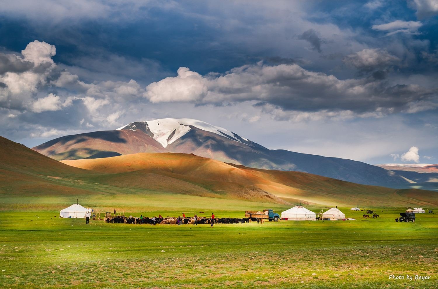 Ger camp in a green valley below a snow-capped mountain